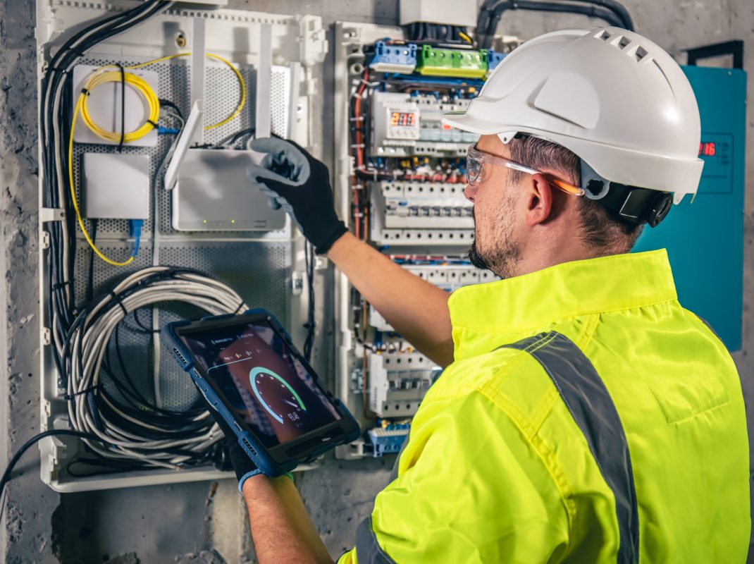 Man, an electrical technician working in a switchboard with fuses. Installation and connection of electrical equipment. Professional uses a tablet.